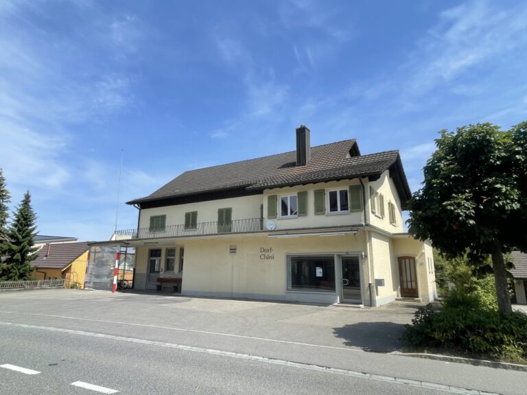 Gebäude der Dorf-Chäsi, alte Käsi, Rickenbach mit heller Fassade, grünen Fensterläden und Balkon im Obergeschoss.