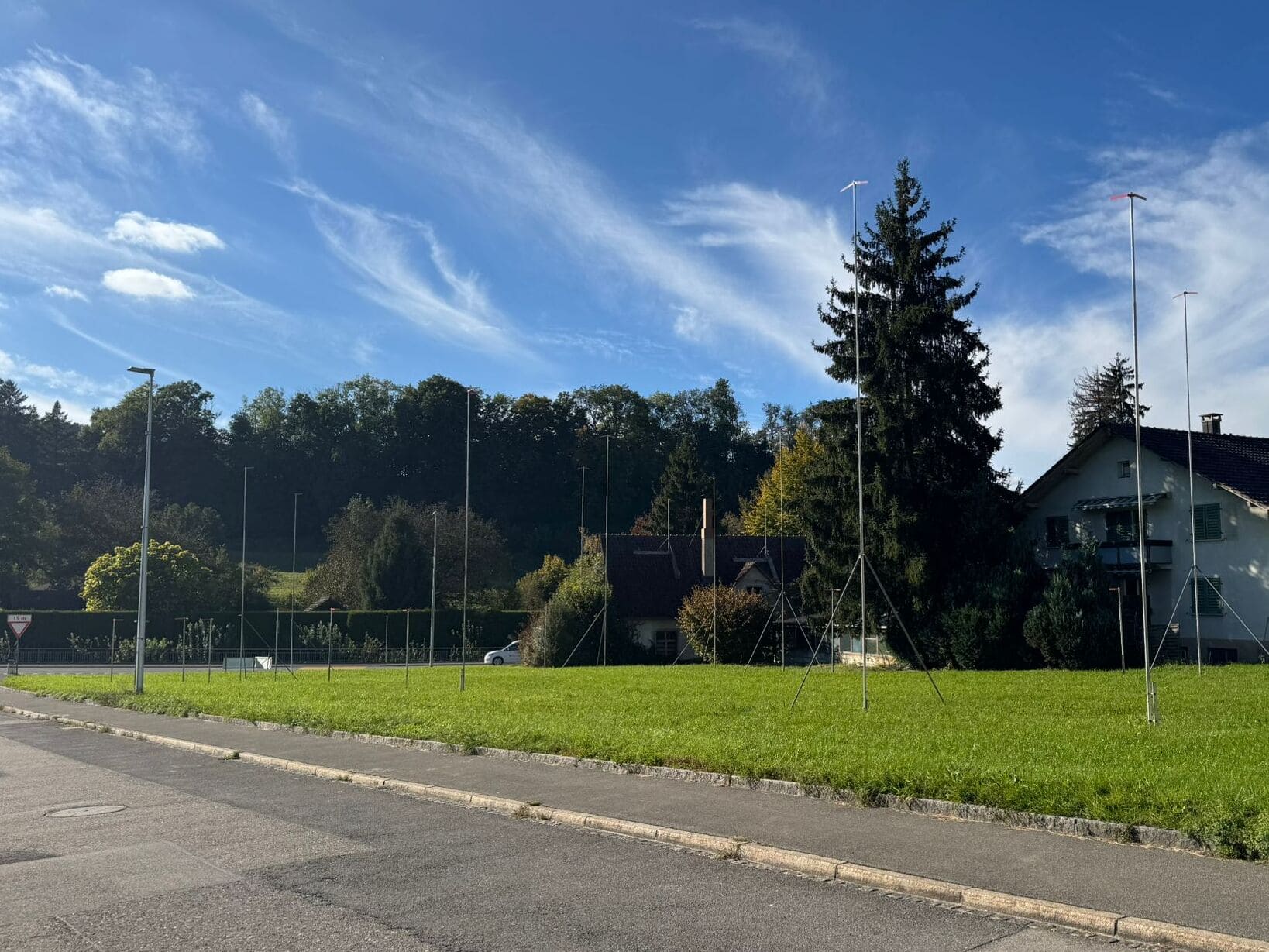 Bauprofile auf einem Grundstück an der Turnhallenstrasse in Gontenschwil markieren die Dimensionen eines geplanten Neubauprojekts. Die freie Grünfläche liegt am Siedlungsrand vor einer bewaldeten Hanglandschaft und veranschaulicht die zukünftige bauliche Entwicklung des Areals.