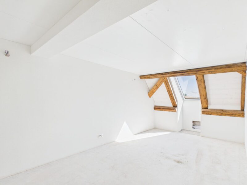 Helles Zimmer einer 2.5-Zimmer-Dachwohnung in der «Gelben Fabrik» mit Dachschräge, sichtbaren Holzbalken und Dachfenster.